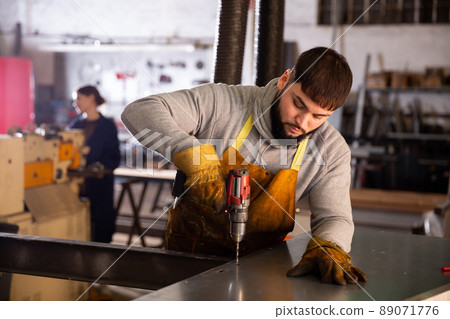 Confident man mechanic drilling metal sheet in workshop Confident man mechanic drilling metal sheet in workshop 89071776