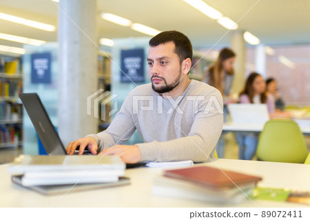 Middle aged man reading books and working on laptop in library 89072411