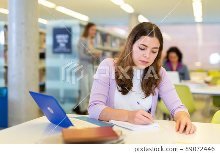 Female student with laptop and books in public library Female student with laptop and books in public library 89072446