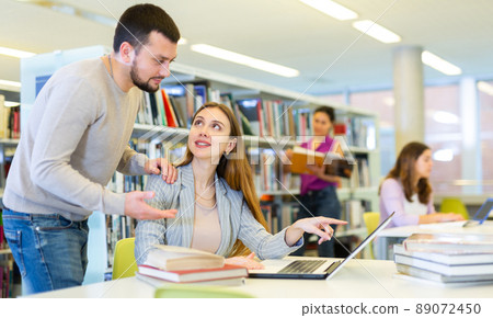 Male librarian helping focused adult student preparing to exam 89072450