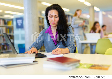Portrait of positive asian woman with laptop in library Portrait of positive asian woman with laptop in library 89072506