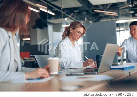 view of smiling multiethnic businesspeople in formal wear at table during conference in office view of smiling multiethnic businesspeople in formal wear at table during conference in office 89073225