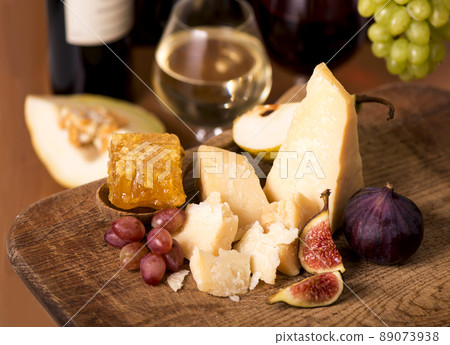 Cheese plate served with grapes, melon, figs, crackers, nuts and white wine on a wooden table 89073938