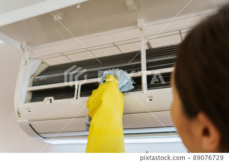 Asian woman cleaning a dirty and dusty air conditioning filter in her house. Housewife removing a dusty air conditioner filter. Asian woman cleaning a dirty and dusty air conditioning filter in her house. Housewife removing a dusty air conditioner filter. 89076729
