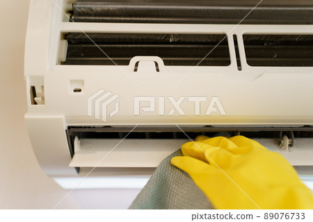 Asian woman cleaning a dirty and dusty air conditioning filter in her house. Housewife removing a dusty air conditioner filter. 89076733