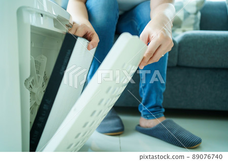 Asian young woman changing - fixing a dirty air purifier HEPA filter after using for a long time. A repairman replacing and installing the air purifier filter. Healthcare and wellbeing. 89076740