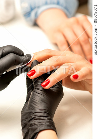 The manicurist finishes the procedure for red nail polishing and cleaning with a cotton napkin, pad, swab in a beauty salon, close up The manicurist finishes the procedure for red nail polishing and cleaning with a cotton napkin, pad, swab in a beauty salon, close up 89078071