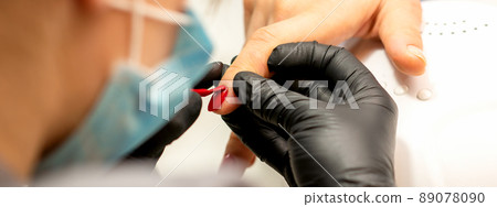 Manicure varnish painting. Close-up of a manicure master wearing rubber black gloves applying red varnish on a female fingernail in the beauty salon 89078090