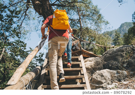 Rear view young adult man climbing a wooden ladder in the mountains. Casually dressed tourist with yellow backpack going up the wooden crafted ladder in the national park with big boulders and cliffs Rear view young adult man climbing a wooden ladder in the mountains. Casually dressed tourist with yellow backpack going up the wooden crafted ladder in the national park with big boulders and cliffs 89078292