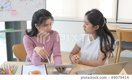 Two female employees in casual clothes are working, discussing ideas for new strategy of development. 89079414