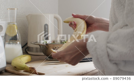 Close-up. Women's hands peel a banana. The girl is preparing a smoothie. 89079436