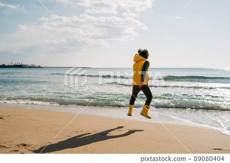 Boy in yellow rubber boots playing with sand at the beach. School kid touching water at autumn winter sea. Child having fun and jumping with waves at the shore. Spring Holiday vacation concept Boy in yellow rubber boots playing with sand at the beach. School kid touching water at autumn winter sea. Child having fun and jumping with waves at the shore. Spring Holiday vacation concept 89080404