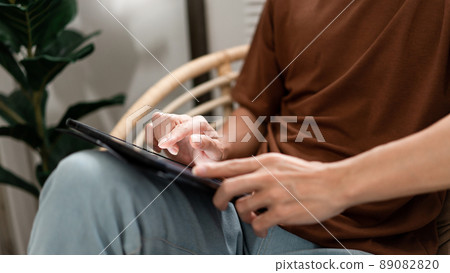 Technology Concept The male with his casual T-shirt and jeans sitting comfortably on the wooden chair and doing touchscreen for checking the web browser on the iPad Technology Concept The male with his casual T-shirt and jeans sitting comfortably on the wooden chair and doing touchscreen for checking the web browser on the iPad 89082820