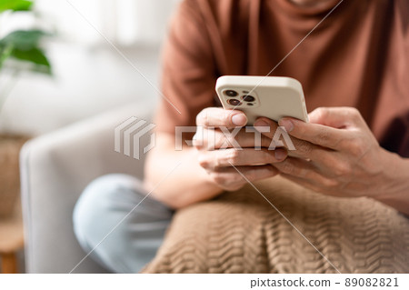 Technology Concept The man sitting next to a pot of plant, putting a small pillow on his lap, and checking something on his smartphone Technology Concept The man sitting next to a pot of plant, putting a small pillow on his lap, and checking something on his smartphone 89082821