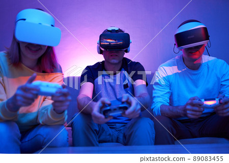 Friends playing virtual reality games using joysticks while sitting on the couch. Friends playing virtual reality games using joysticks while sitting on the couch. 89083455