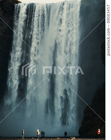 Skogafoss iconic waterfall with tourists under the stream Skogafoss iconic waterfall with tourists under the stream 89083457