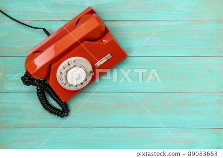 Old, orange rotary dial telephone on blue wooden background 89083663