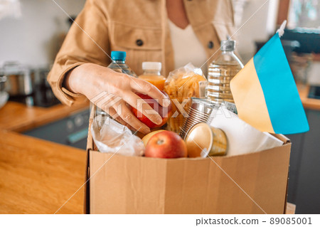 Volunteer person packing a paper box with humanitarian aid for ukrainian refugees. Charity, donation and volunteering concept  89085001