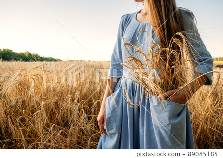 Ukrainian woman in blue linen dress with wheat spikelets on wheat fields. War in Ukraine threatens global wheat supply Ukrainian woman in blue linen dress with wheat spikelets on wheat fields. War in Ukraine threatens global wheat supply 89085185