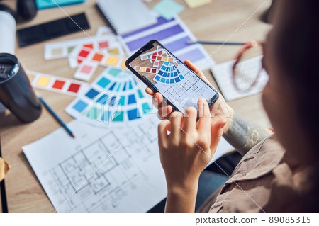Close up shot of woman taking a photo of a blueprint and color samples palette using smartphone while working on new interior design project in her office 89085315