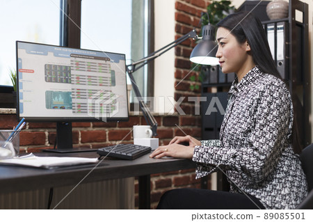 Research agency office worker analyzing organization financial data and statistics. Young confident company employee reviewing startup project status charts while sitting in modern office. 89085501