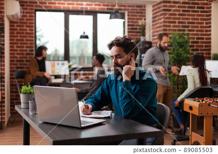 Businessman talking with leader into headphones writing marketing strategy on clipboard while planning business collaboration in startup office. Entrepreneur man working at management project Businessman talking with leader into headphones writing marketing strategy on clipboard while planning business collaboration in startup office. Entrepreneur man working at management project 89085503