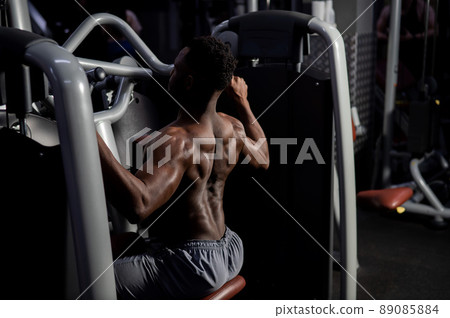 Shirtless african american man doing back exercises on a machine in the gym. 89085884