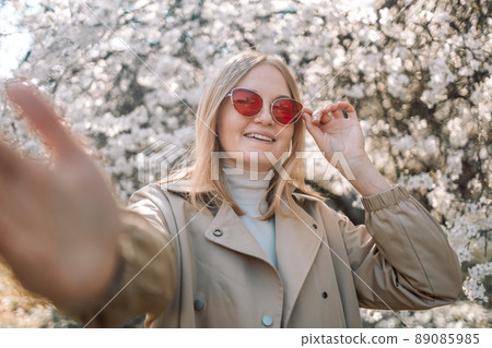 Close-up portrait of happy caucasian cheery young blond girl in red stylish sunglasses taking selfie in park at spring time Close-up portrait of happy caucasian cheery young blond girl in red stylish sunglasses taking selfie in park at spring time 89085985