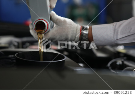 Auto mechanic refueling and pouring oil into engine motor ia car 89091238