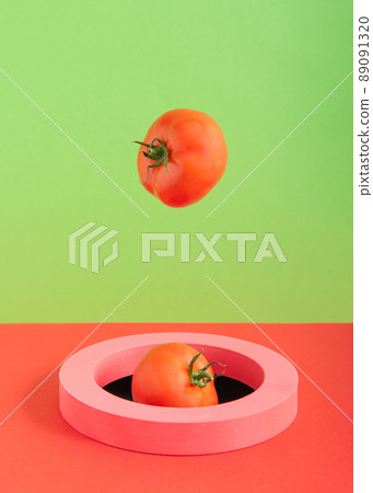 Tomatoes fall into the hole through a pink ring on a green and red background 89091320