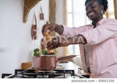 Plus size african woman in pink clothes cooking in the kitchen Plus size african woman in pink clothes cooking in the kitchen 89091508