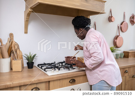 Plus size african woman in pink clothes cooking in the kitchen Plus size african woman in pink clothes cooking in the kitchen 89091510