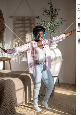 Contented african woman in light clothes listening to music and dancing 89091521
