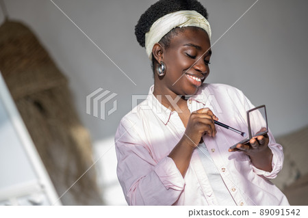 Contented african woman in light clothes holding powder in hands Contented african woman in light clothes holding powder in hands 89091542