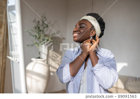 Contented african woman in light clothes near the mirror Contented african woman in light clothes near the mirror 89091563