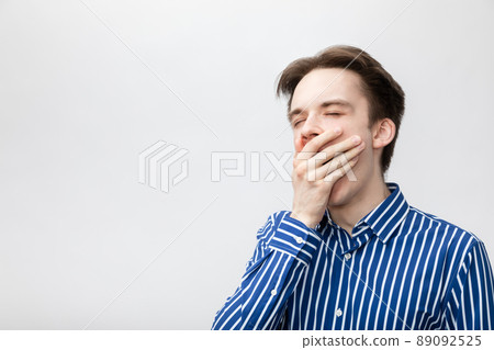 Yawning young man studio shot on gray background Yawning young man studio shot on gray background 89092525