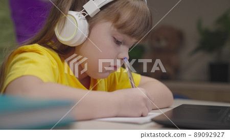 little schoolboy student writes mathematics notebook. child kid solves difficult learning problems. child education program. girl headphones with digital laptop writes notebook. study work home desk. 89092927