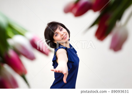 An adult brunette in a blue blouse on a white background with bright red juicy tulips An adult brunette in a blue blouse on a white background with bright red juicy tulips 89093631