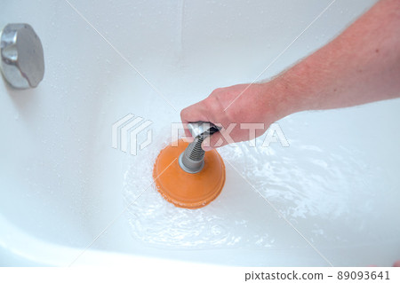 A man's hand holds an orange bright plunger, cleaning the bath A man's hand holds an orange bright plunger, cleaning the bath 89093641