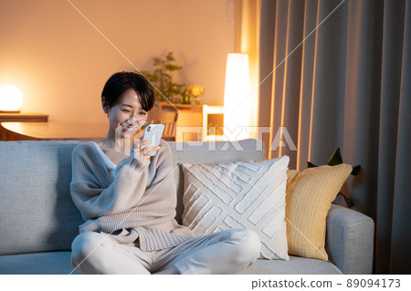 A woman relaxing at home at night (smartphone, email, internet) 89094173