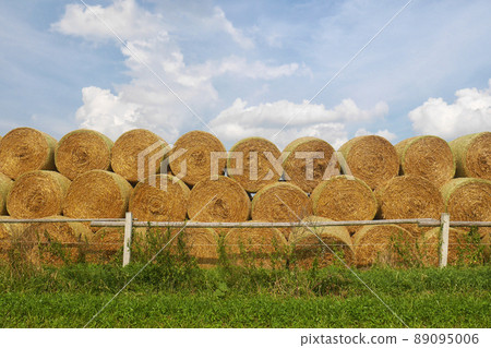 stack of straw bales - stacked round straw bales, meadow with wooden fence in foreground 89095006