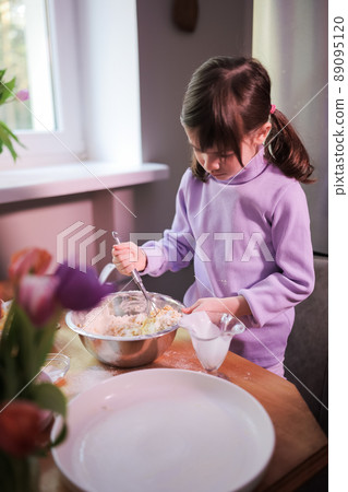 Daughter knead the dough in the kitchen.  89095120