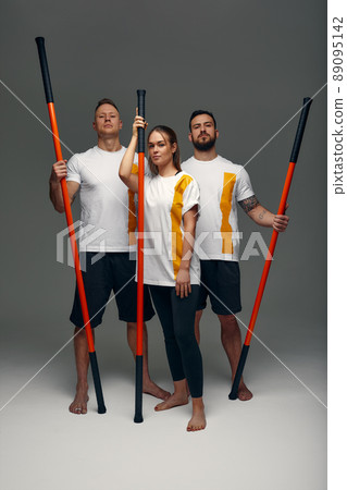 Two men and woman aikido fighters with wooden fight stick posing in studio, fight demonstration 89095142