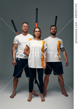 Two men and woman aikido fighters with wooden fight stick posing in studio, fight demonstration Two men and woman aikido fighters with wooden fight stick posing in studio, fight demonstration 89095143