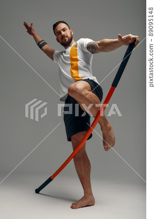 A fighter in white t-shirt and black shorts, stands in a fighting artificially pose and holds a fight stick on studio background. 89095148