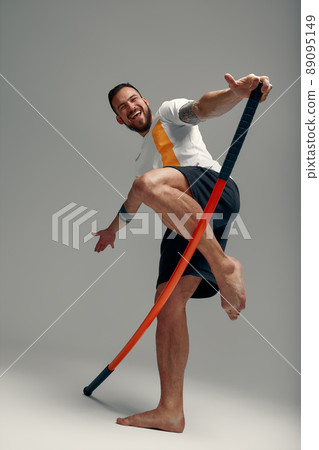 A fighter in white t-shirt and black shorts, stands in a fighting artificially pose and holds a fight stick on studio background. A fighter in white t-shirt and black shorts, stands in a fighting artificially pose and holds a fight stick on studio background. 89095149