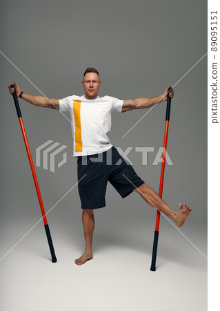 A fighter in white t-shirt and black shorts, stands in a fighting artificially pose and holds a fight stick on studio background. A fighter in white t-shirt and black shorts, stands in a fighting artificially pose and holds a fight stick on studio background. 89095151