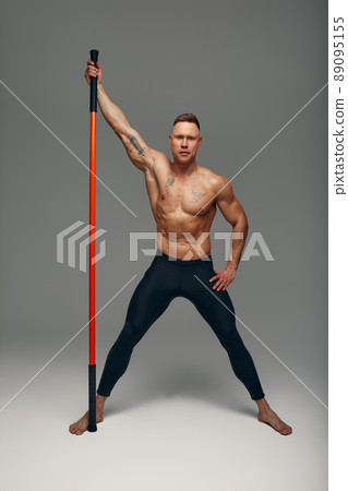 A fighter shirtless in black shorts, stands in a fighting artificially pose and holds a fight stick on studio background. A fighter shirtless in black shorts, stands in a fighting artificially pose and holds a fight stick on studio background. 89095155