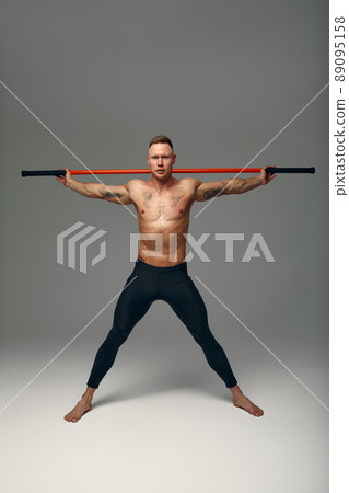 A fighter shirtless in black shorts, stands in a fighting artificially pose and holds a fight stick on studio background. A fighter shirtless in black shorts, stands in a fighting artificially pose and holds a fight stick on studio background. 89095158