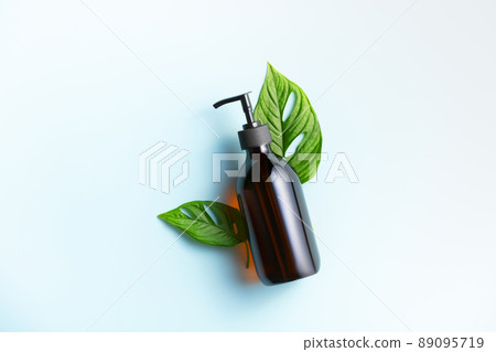 Banner. One cosmetic dark amber glass bottle with green plant on blue background Banner. One cosmetic dark amber glass bottle with green plant on blue background 89095719